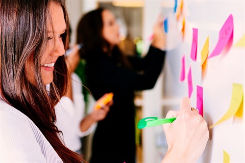Close up of young woman writing an idea on a post-it and placing it on a whiteboard