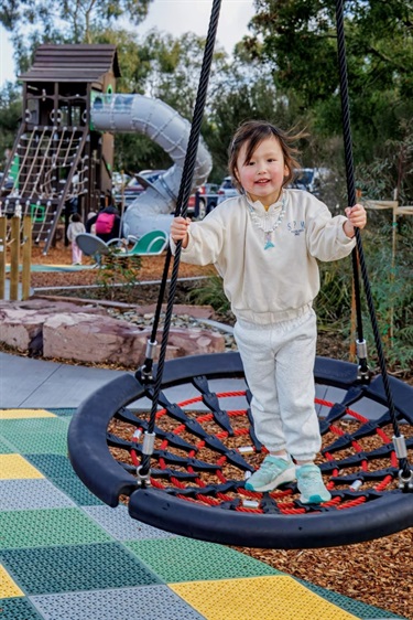 Young child on a nest swing with giant slide in the background