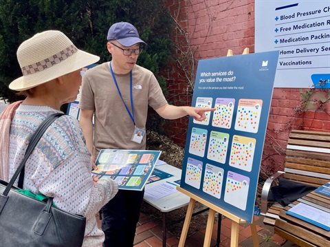 Council staff member speaking with a community member at a budget consultation pop-up, using a dot-voting board to identify which council services are most valued.