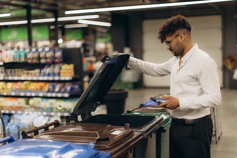 Man standing in front of bins sorting recycling at a store