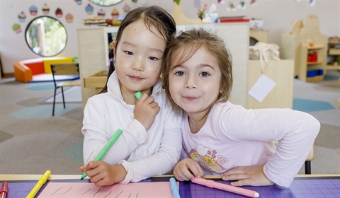 Two kindergarten children sitting at a desk, facing the camera together
