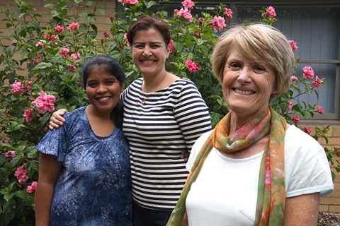 Rosemary Snibson photographed with two other people standing in front of rose bush