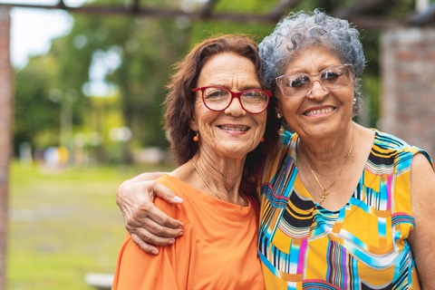 Two older women smiling at camera with their arms around each other