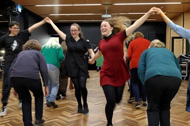 Celtic dancers moving together through a set formations, laughing and enjoying themselves.