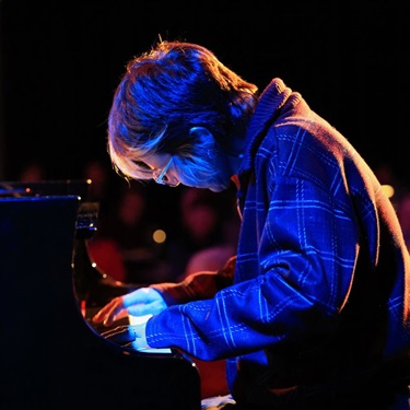 Close up of a piano player, deep in concentration, lit by a blue light.