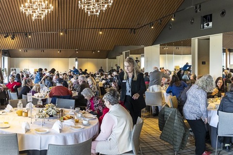 A room full of people seated around circular tables celebrating a morning tea during Monash Seniors Festival