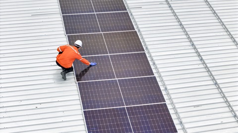 worker inspects solar panels on metal roof